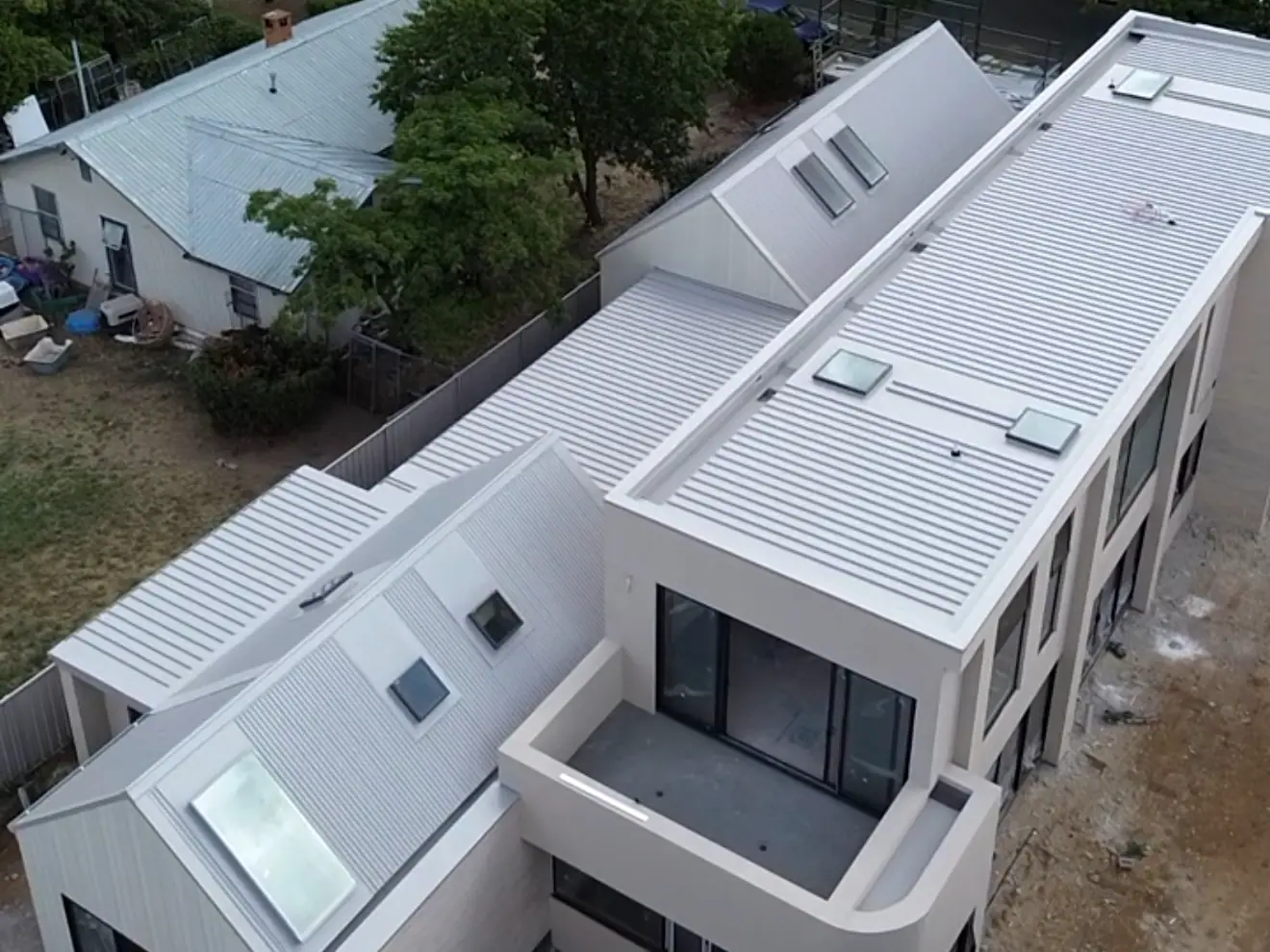 Drone view of a pale two storey home with light metal roofing, vertical wall cladding and skylights
