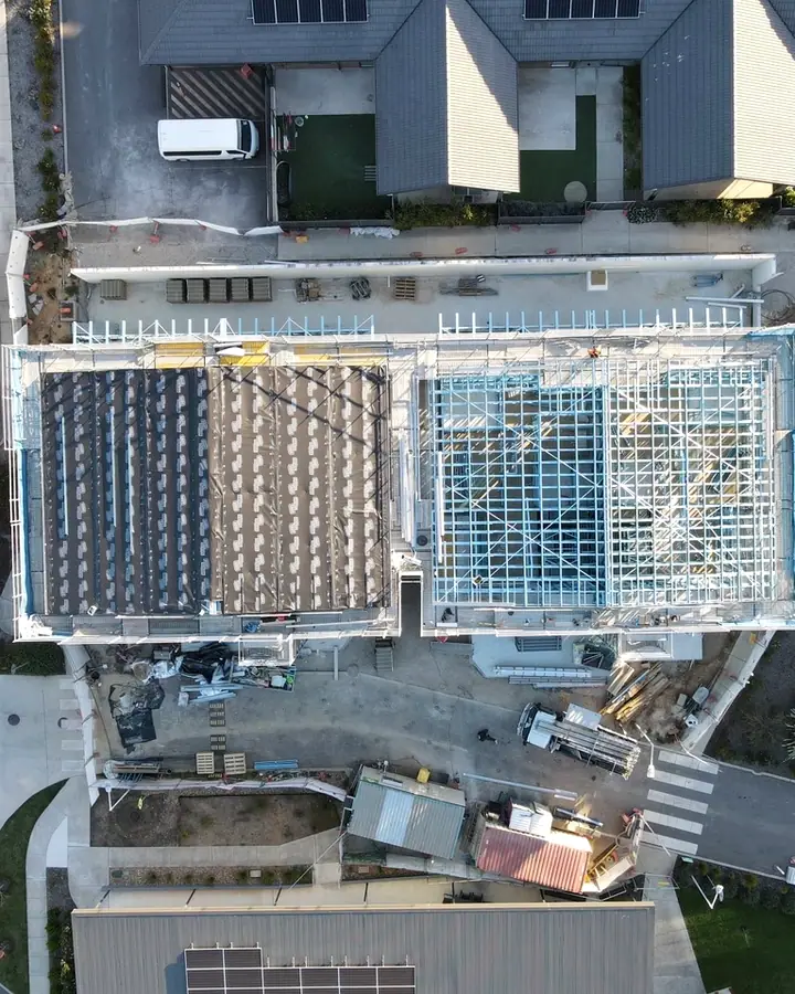 Top down drone view of a commercial building mid install, one roof under blanket and battens, the next in steel frame