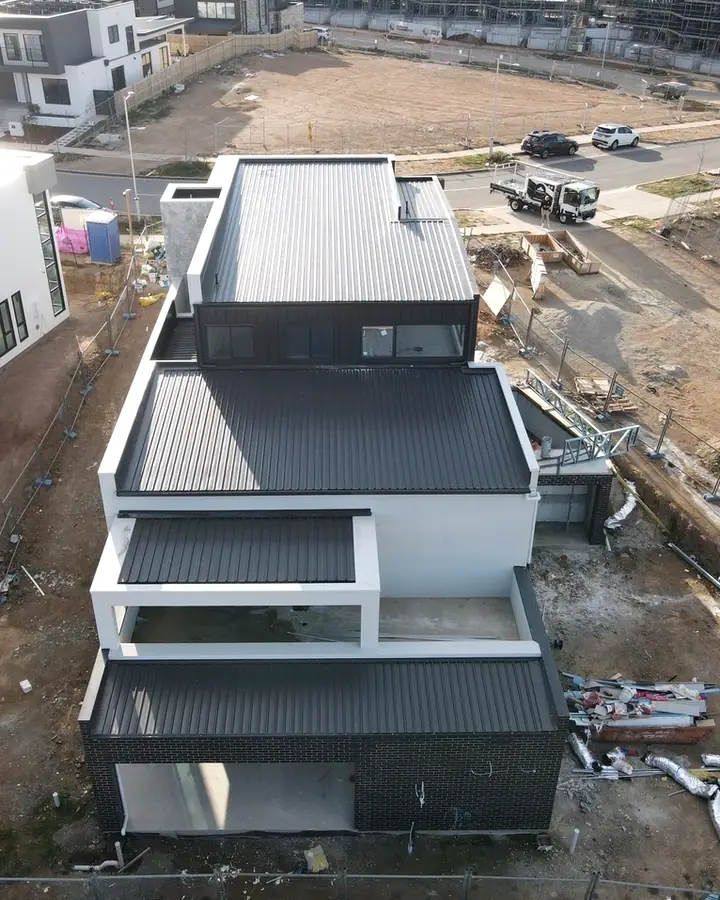 Drone view of a white rendered three level home with dark ribbed metal roofs on each level