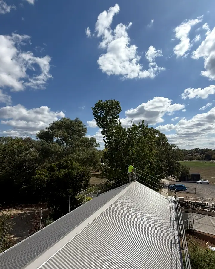 A Cloudbreak roofer standing on the ridge of a long silver corrugated gable roof, with edge protection along the eaves